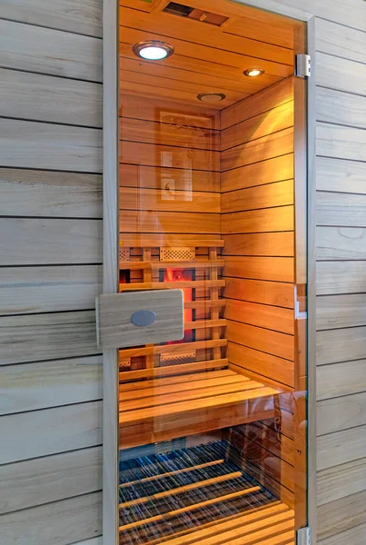 view into a wooden infrared cabin with glowing heating elements and closed glass door