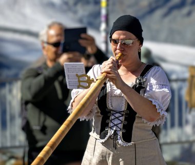 Bir bayan müzisyen, İsviçre 'nin Valais kantonunda Gornergrat' taki çark demiryolu platosu üzerinde turistlerin önünde geleneksel bir alphorn çalıyor..