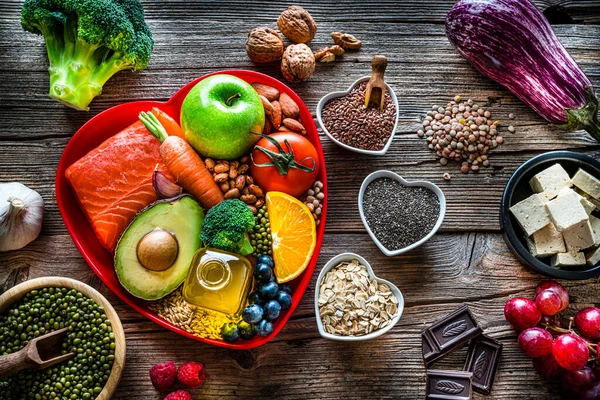Healthy eating: group of fresh multicolored foods to help lower cholesterol levels and for heart care shot on wooden table. The composition includes oily fish like salmon. Beans like Pinto beans and brown lentils. Vegetables like garlic, avocado.