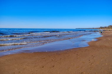 Yazın kumsalda mavi su dalgaları, kayalar ve çakıl taşlarıyla kumlar.