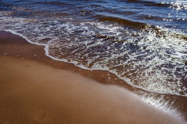 Yazın kumsalda mavi su dalgaları, kayalar ve çakıl taşlarıyla kumlar.