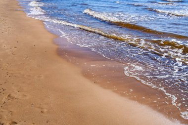 Yazın kumsalda mavi su dalgaları, kayalar ve çakıl taşlarıyla kumlar.