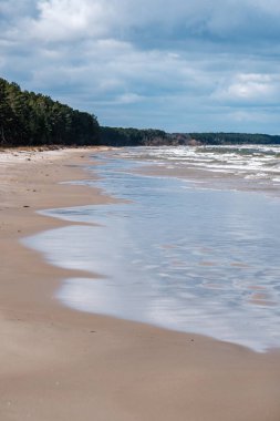 Fırtınadan önce beyaz kum ve mavi suyla deniz kıyısı. Beyaz başlı dalgalar