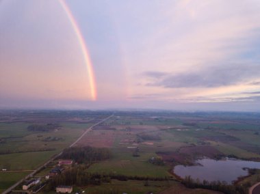 Yağmur fırtınasından sonra kırsal yolların üzerinde güzel gökkuşağı. kırmızı bulutlu gökyüzü
