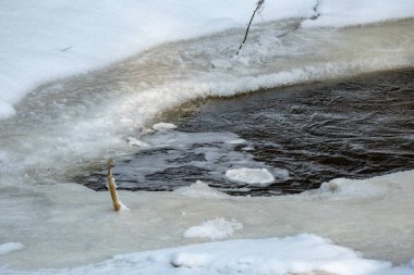 Buz, kar ve buzun altındaki kahverengi suyla ormandaki donmuş nehir manzarası. Kırsal kesimde kış yağmuru