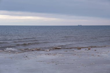 Denize yakın, donmuş kum ve suda buz blokları olan buzlu kış plajı. Soğuk kum tepeleri