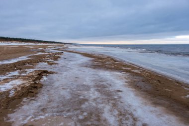 Denize yakın, donmuş kum ve suda buz blokları olan buzlu kış plajı. Soğuk kum tepeleri