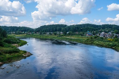 Geniş nehir manzarası geniş su kütlesi, gökyüzünün mavi yansımaları ve arka planda yeşil ağaçlar.