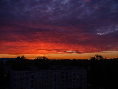 Şehir çatıları üzerinde dramatik renkler ve bulutlarla koyu renkli günbatımı