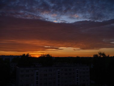 Şehir çatıları üzerinde dramatik renkler ve bulutlarla koyu renkli günbatımı