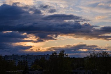 Şehir çatıları üzerinde dramatik renkler ve bulutlarla koyu renkli günbatımı