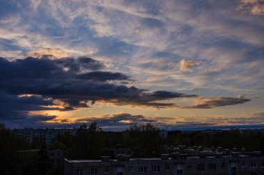 Şehir çatıları üzerinde dramatik renkler ve bulutlarla koyu renkli günbatımı