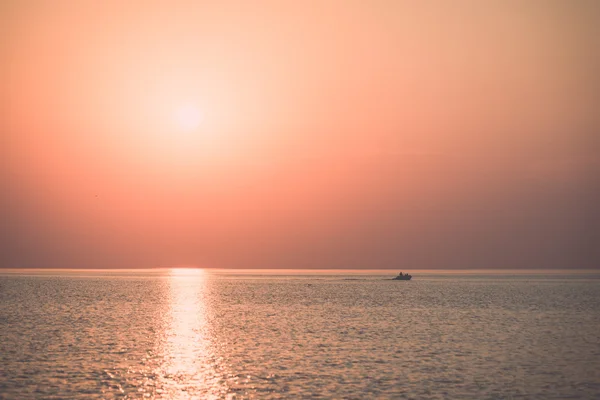 Boot in de zonsondergang in de zee met reflecties en wolken - retr op te geven — Stockfoto