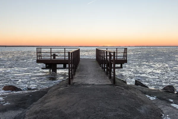 Sunset over frozen sea with old metal bridge — Stock Photo, Image