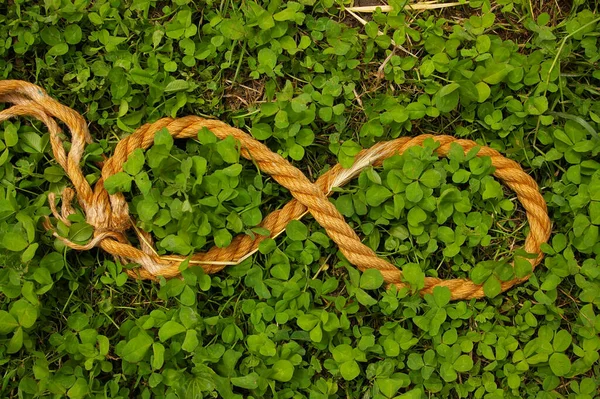 Organic hemp rope arranged in the form of the symbol of infinity. Endless symbol made from natural rope on a green clover background. — Stock Photo, Image