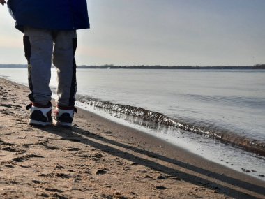 Sonbaharda sıcacık giysiler içinde nehir kıyısında yürüyen bir çocuk.