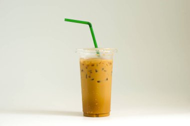 Şeffaf plastik bardakta buzlu kahve ve beyaz arka planda yeşil pipet..