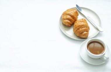 Beyaz seramik bardakta sıcak kahve fincanı yuvarlak beyaz seramik bardaklar ve taze kruvasanlarla yuvarlak seramik tabakta paslanmaz çelik bıçağa karşı..