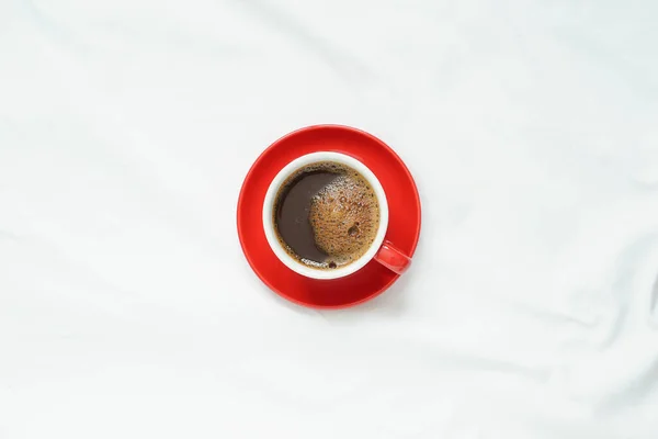 top view of hot coffee in red ceramic cup on red ceramic plate placed on blank clean tablecloths with soft light in the morning