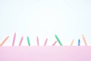 Beyaz arkaplanda renkli doğum günü mumlarının ve kopyalama alanı olan pembe kağıtların üst görünümü.