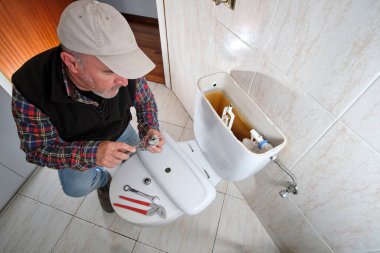 Tesisatçı tuvalet sifonunu tamir ediyor.