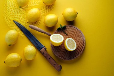 Yukarıdan ikiye bölünmüş limon manzarası, kırsal bıçak ve sarı arka planda taze limon.