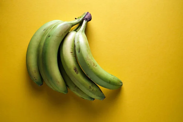 Bunches of green bananas on a yellow background