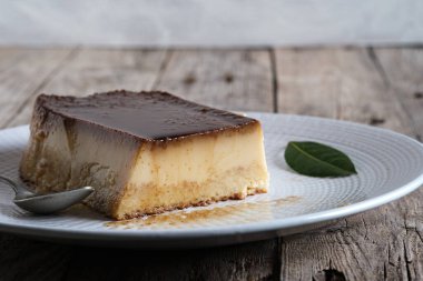 Karamelli puding, beyaz tabakta ev yapımı ve ahşap masa..