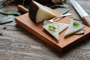 Ahşap bir tahtanın üzerinde rustik arka planda kesilmiş Manchego peyniri dilimleri.
