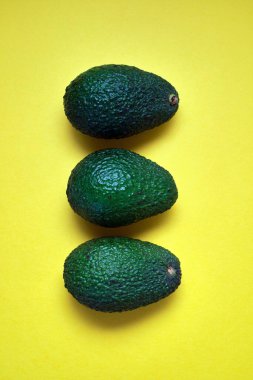 Yukarıdan görülen sarı arka planlı üç çiğ avokado.