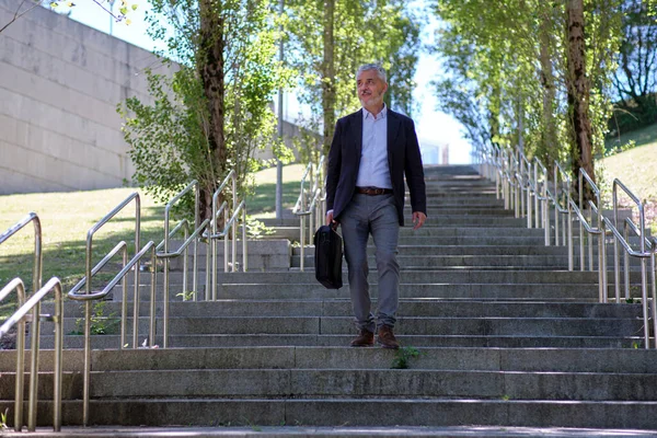 Happy 60-year-old businessman walking down some stairs on the street