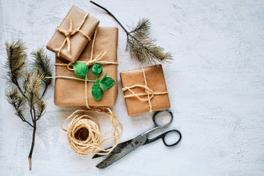 Kraft kağıdına sarılı hediye paketleri jüt, makas ve iple beyaz desenli bir zemine bağlanmış. Üst görünüm.
