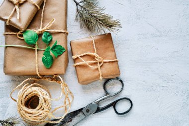 Kraft kağıdına sarılı hediye paketleri jüt, makas ve iple beyaz desenli bir zemine bağlanmış. Üst görünüm.