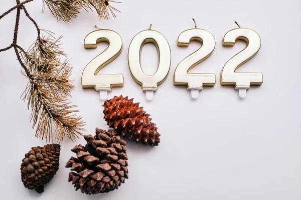 Yeni yıl 2022. Mumlar, hediye paketleri ve beyaz arka planda kurumuş çam kozalakları ile yazılmış.