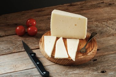 Taze peynir dilimlere ayrılır ve ahşap bir tahtaya yerleştirilir. Taze domatesler yakınlarda dinleniyor ve bıçak servis için kullanılıyor..