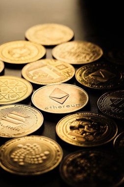 Birkaç kripto para birimi bir masanın üzerine yerleştiriliyor. Her sikkenin kendine has bir tasarımı var. Sikkeler ışığı yansıtıyor ve Ethereum 'u vurgulayarak farklı sembol ve logolar gösteriyor..