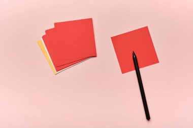 Kırmızı ve sarı kağıtlar bir tarafa istiflenir ve siyah bir kalem tek bir kırmızı karenin yanına yerleştirilir. Arka plan pembe, basit bir çalışma alanı oluşturuyor..