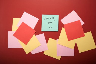 Kırmızı arka planda renkli yapışkan notların bir koleksiyonu düzenlenir. Yeşil bir notta gülen yüzlü bir teşekkür mesajı var..