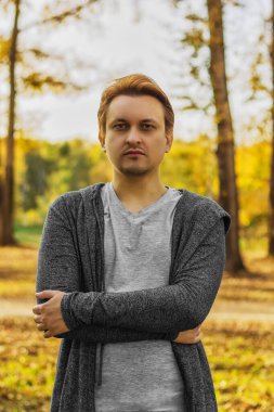 Parkta güneşli bir sonbahar günü. Çekici genç adam ayakta kameraya bakıyor.