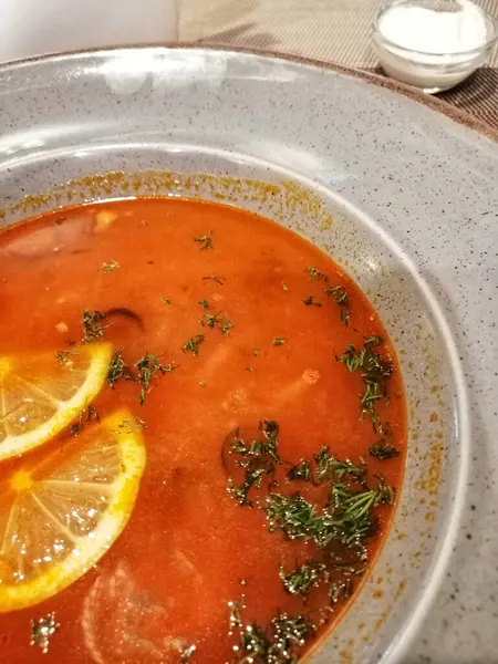 Limon dilimli çorba, ekşi kremalı bir kasenin yanında sebze solynka..