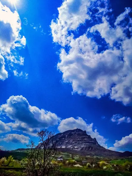 Mavi gökyüzü ve bulutların arka planında, yeşil genişliğe sahip dağlık bir alan..