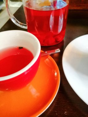 Koyu bir ahşap masa, bir çay çifti, bir fincan ve çay tabağı, ve beyaz bir tabağın kenarındaki meyve suyu ile berrak bir cam bardak.