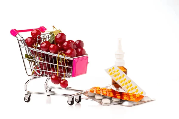Vedle léků je vozík v supermarketu naplněn zralými červenými třešněmi. Koncept na téma zdravého životního stylu, vitamínů a správné výživy. — Stock fotografie
