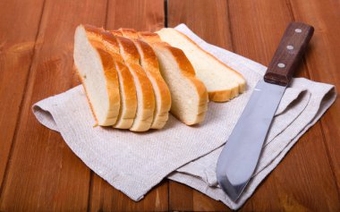 Pieces of bread on a linen napkin near a knife. Wooden table