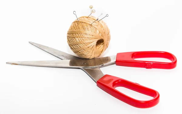 Scissors with red handles and a ball of beige threads with pins, — 스톡 사진