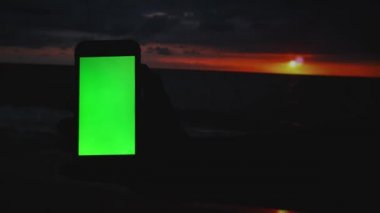 Gün batımında akıllı telefonu elinde tutan adam.