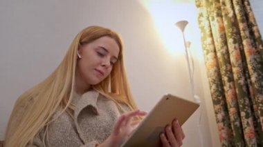 Mutlu gülümseyen genç kadın kanepede oturuyor, arkadaşı tablet kullanarak arıyor.