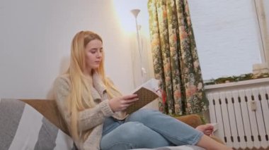 Genç bir kadın sandalyesinde rahatlıyor ve kitabı karıştırıyor..