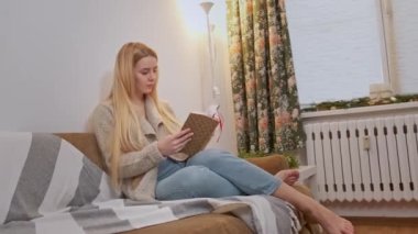 Genç bir kadın sandalyesinde rahatlıyor ve kitabı karıştırıyor..