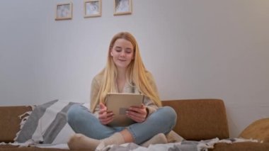 Kanepede oturan, internette sörf yapan ve dijital tablette dans eden genç bir kadın..